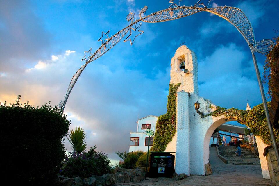 Un arco de piedra blanca cubierto de hiedra, que da paso a un edificio con una torre de campanas.