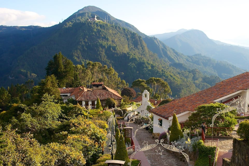 Un pueblo con arquitectura tradicional, rodeado de montañas verdes exuberantes y una iglesia destacada.