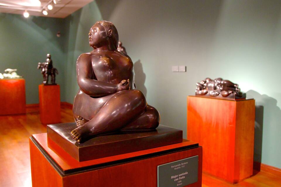 En bronsstaty som föreställer en sittande kvinna, placerad på en piedestal i ett museum.