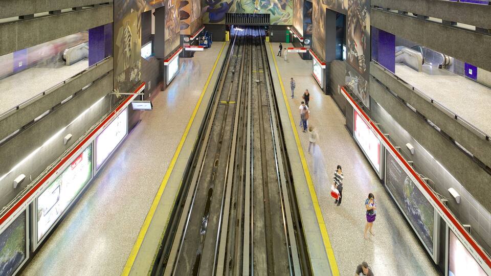 A subway station with multiple tracks, overhead signage, and advertisements.
