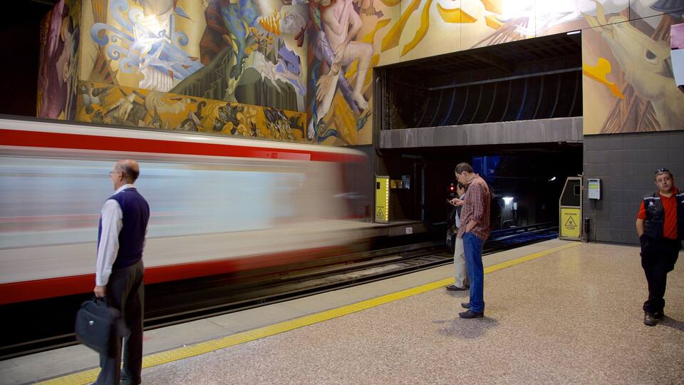 A subway station with a mural on the wall and a train passing by.