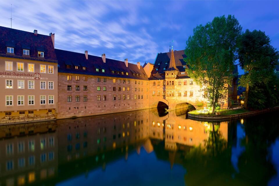Een historische Europese stad met een rivier, spiegelende gebouwen en een brug.