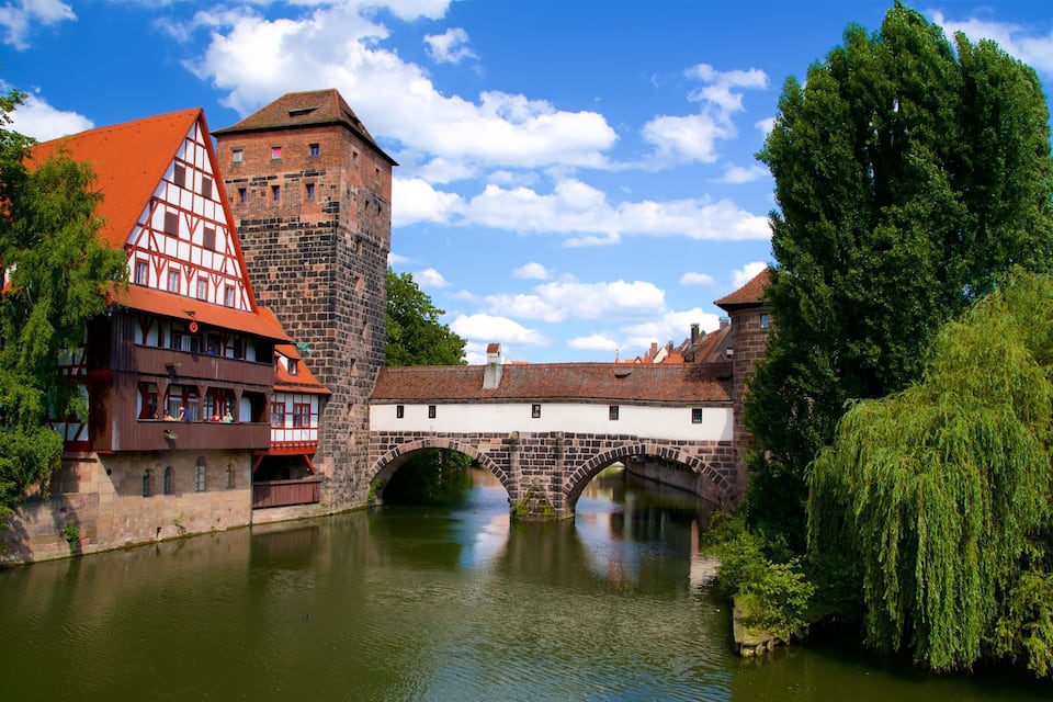 Un pueblo histórico con un río, un puente y casas tradicionales de entramado de madera.