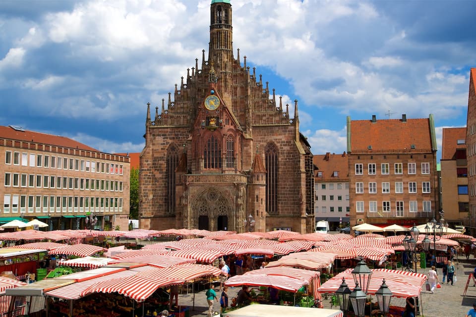 Een historisch kerkgebouw met een klokkentoren, omringd door marktkramen met rood-witte tenten.