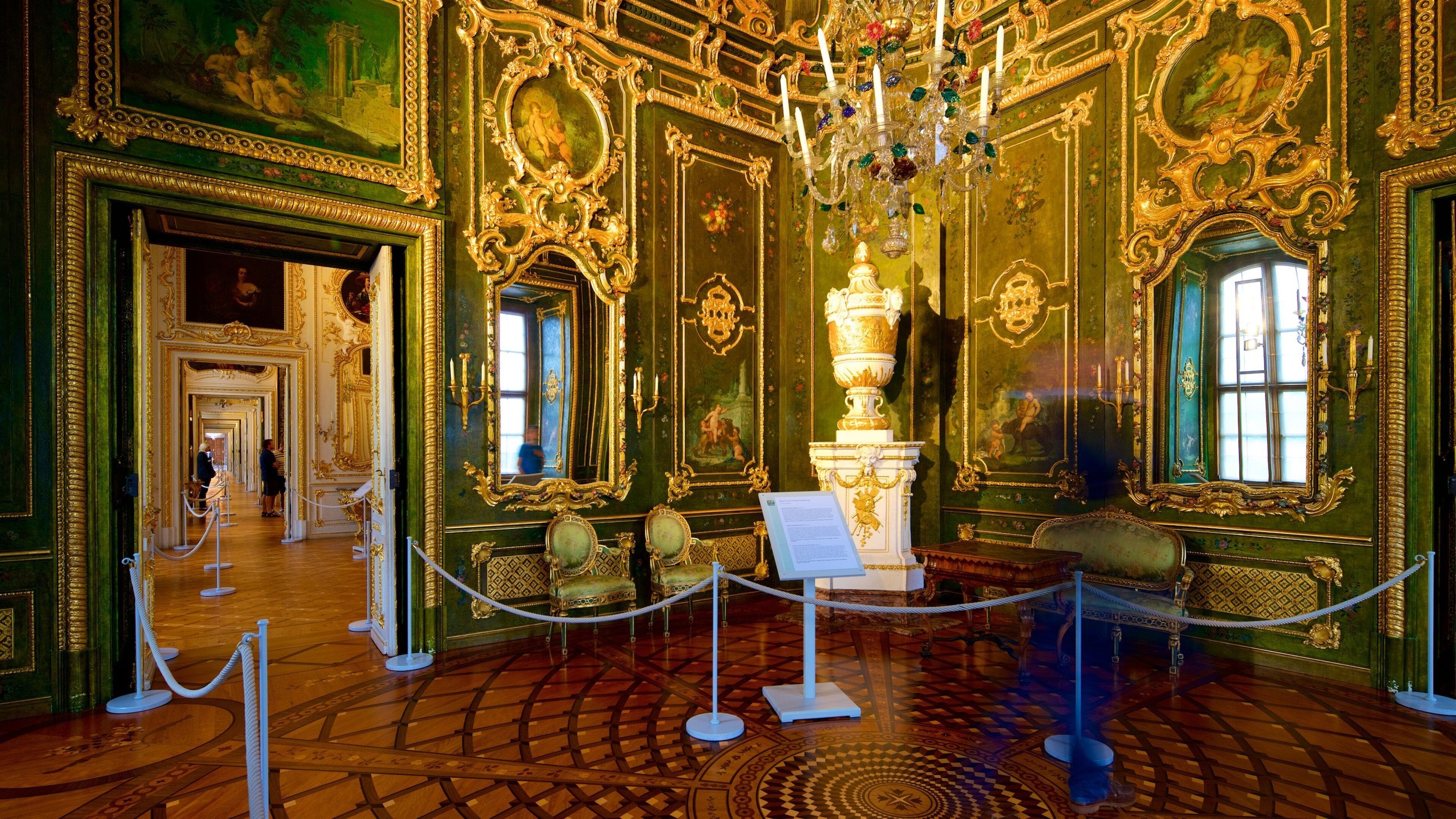 Una habitación opulenta con detalles en oro ornamentales, un candelabro y un espejo grande.