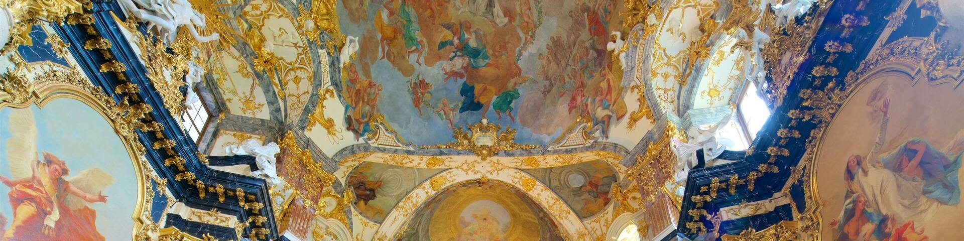 An ornate interior with gold accents, marble columns, and elaborate ceiling frescoes.