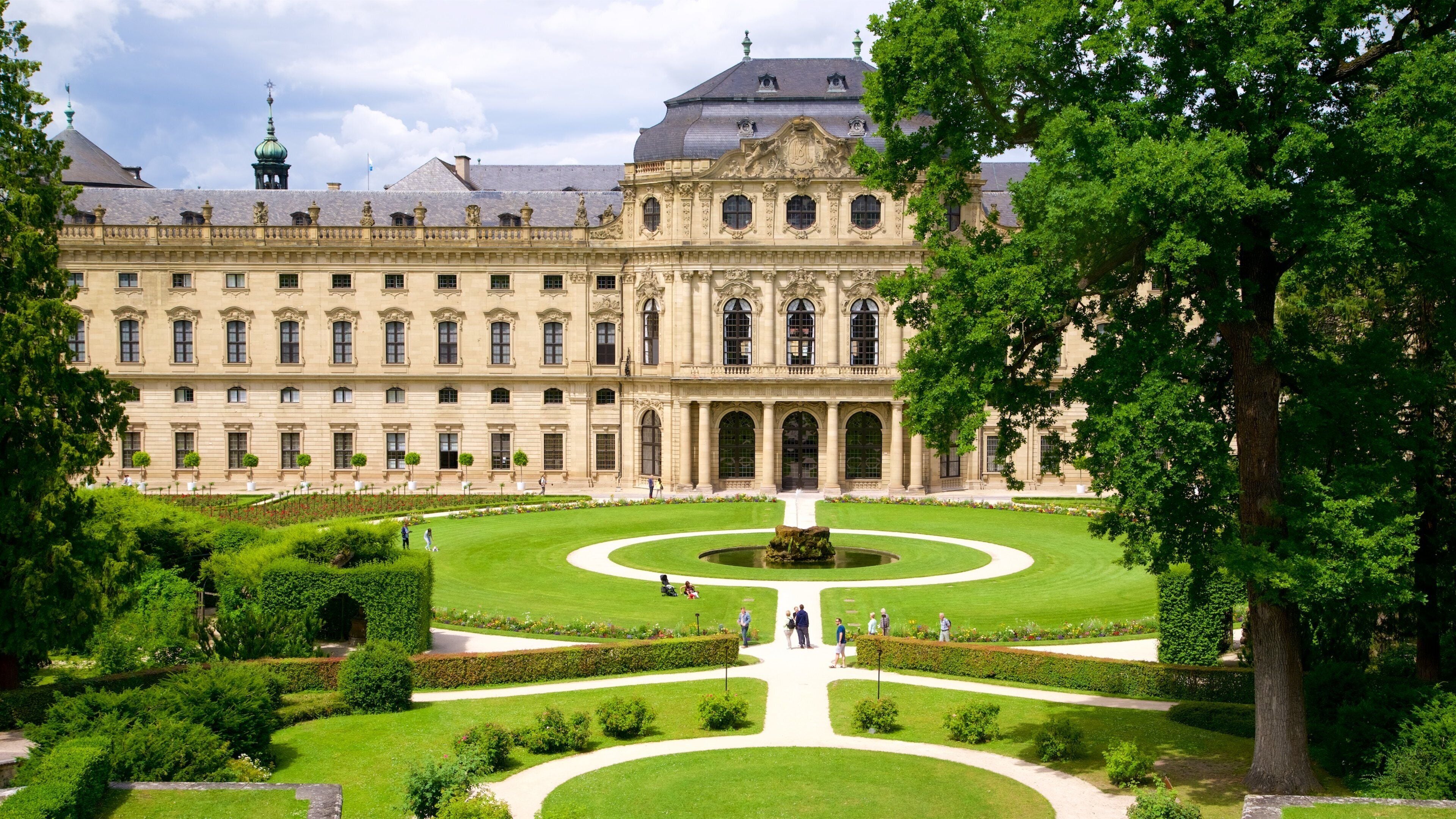Un palacio imponente con un jardín simétrico, que presenta una fuente central y céspedes cuidados.
