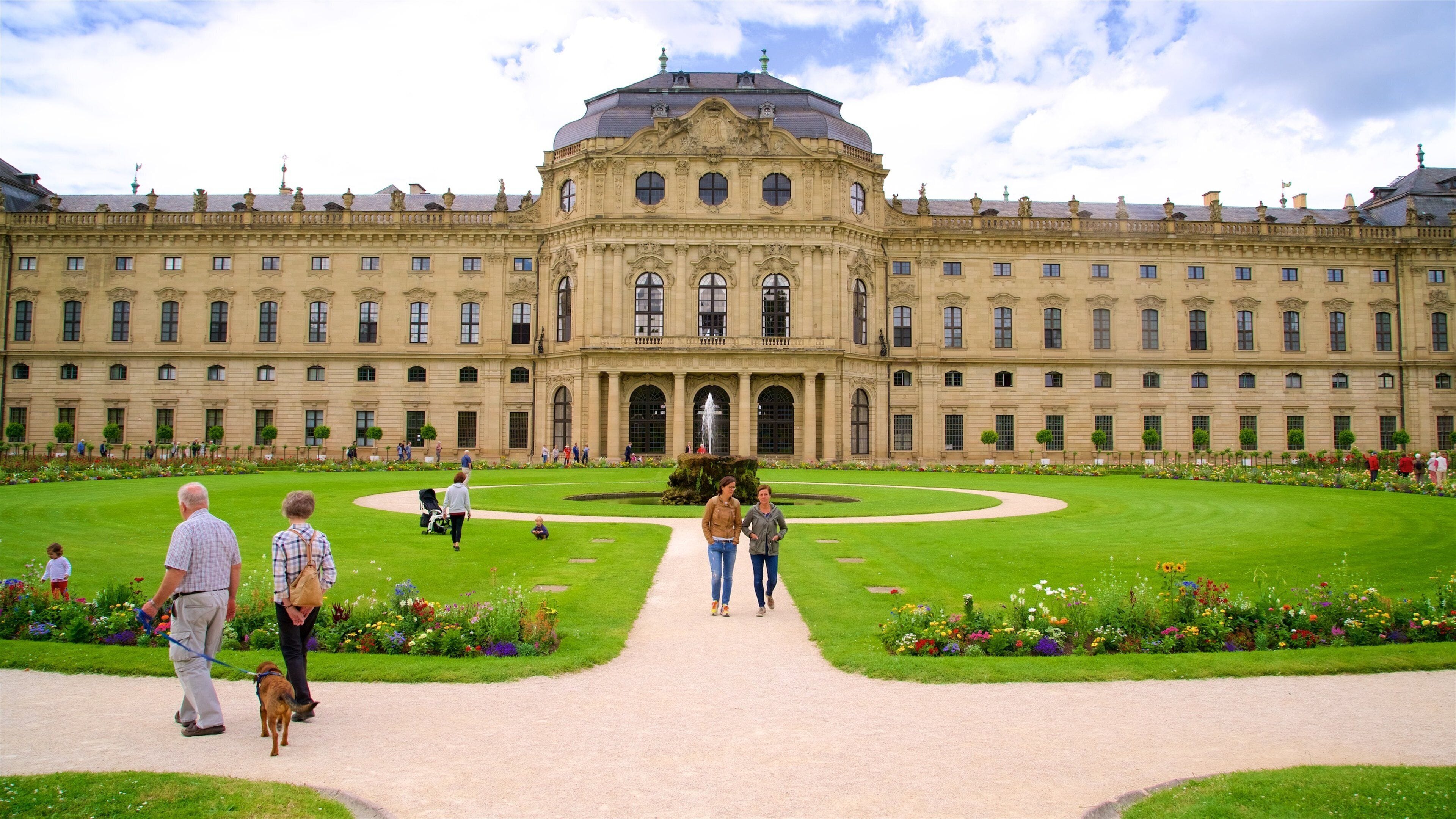 A large, ornate building with a central dome and symmetrical wings, surrounded by a well-manicured garden with a central fountain.
