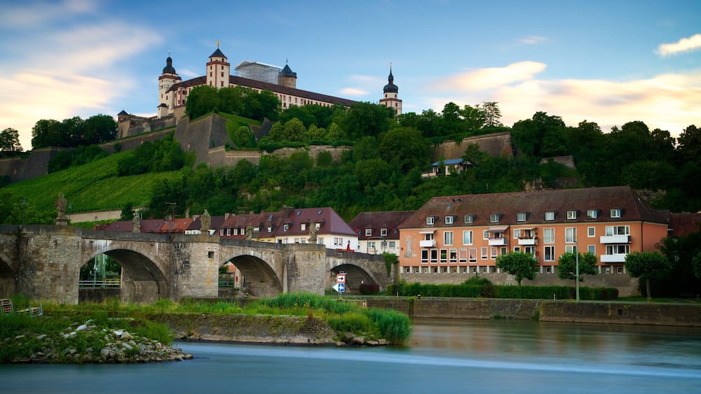 A historic castle on a hill, a stone bridge, and residential buildings along a river.
