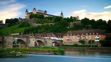 Um castelo histórico numa colina, uma ponte de pedra e edifícios residenciais ao longo de um rio.