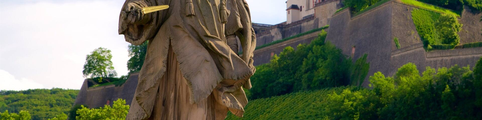 A statue of a historical figure holding a sword, with a castle and lush greenery in the background.
