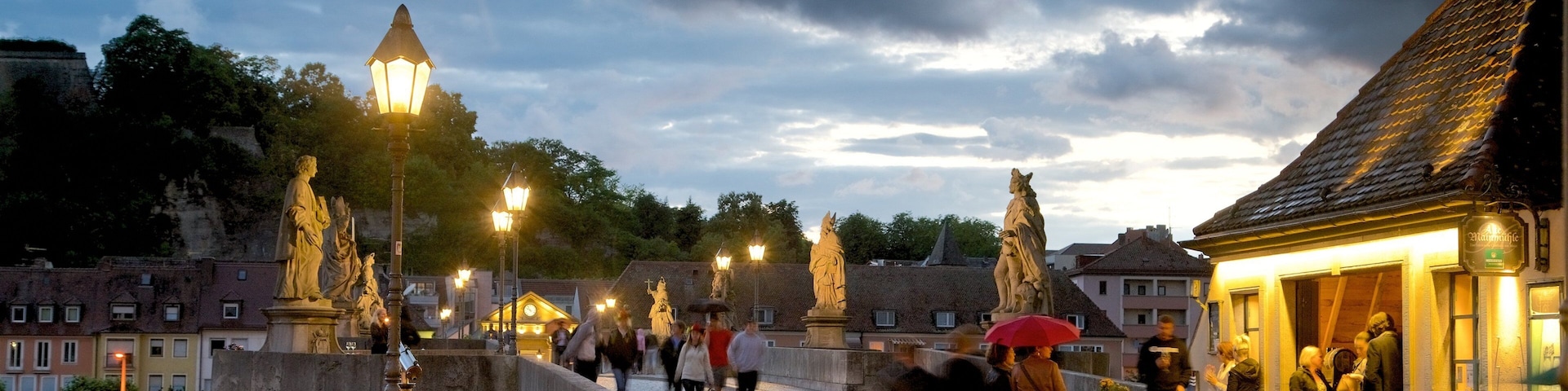 Un puente histórico flanqueado por edificios, un río y faroles, con estatuas.