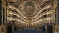 An ornate theater with intricate ceiling frescoes and golden chandeliers.