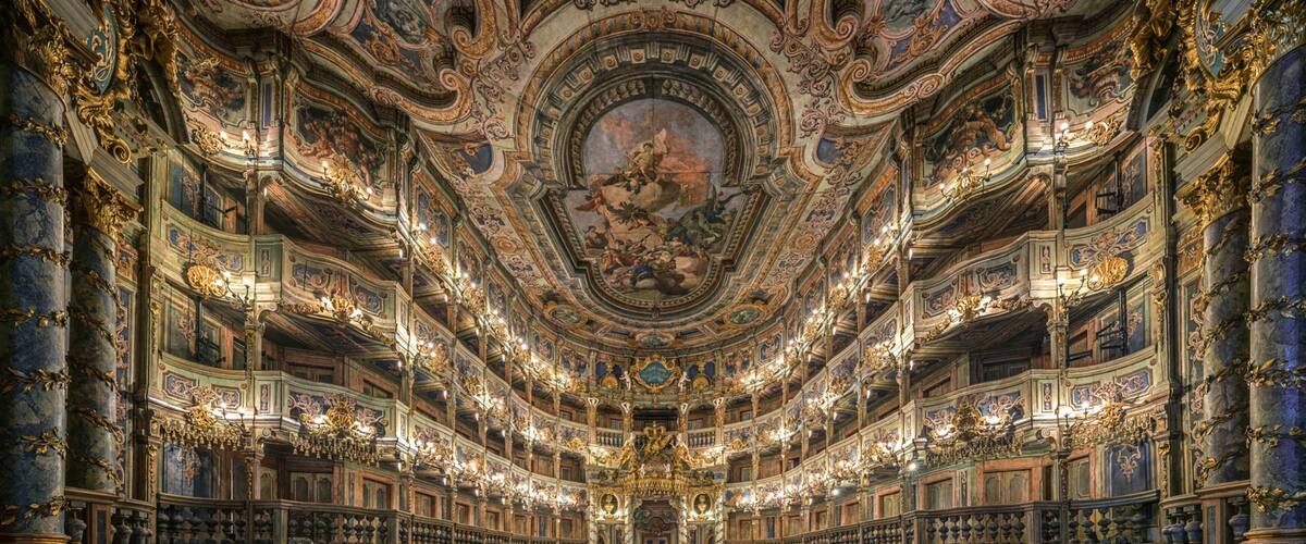 An ornate theater with intricate ceiling frescoes and golden chandeliers.