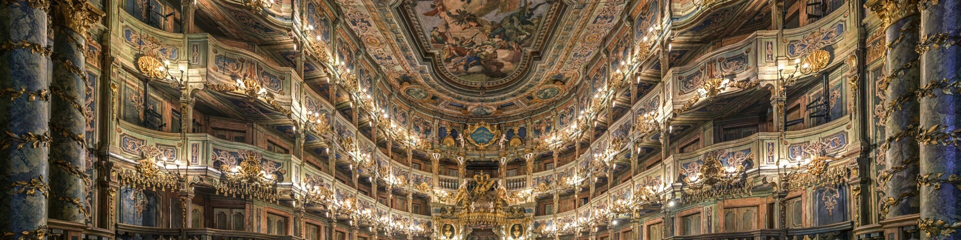 An ornate theater with intricate ceiling frescoes and golden chandeliers.