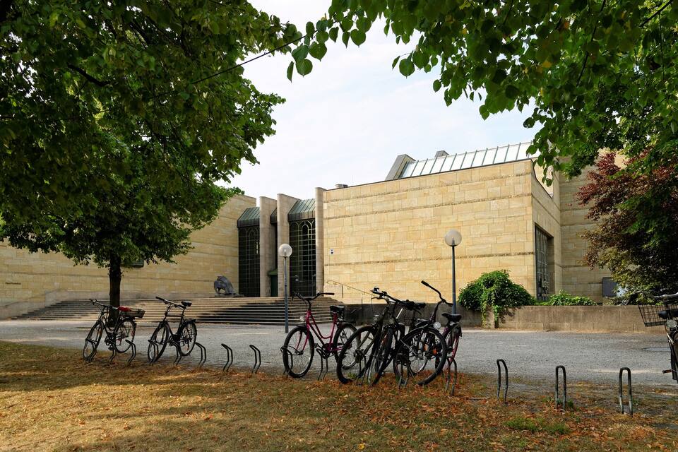 A building with a modern design, surrounded by trees and a bicycle parking area.