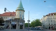 A historic tower with a green spire, a street with parked cars, and a building with a sign for Oktoberfest.