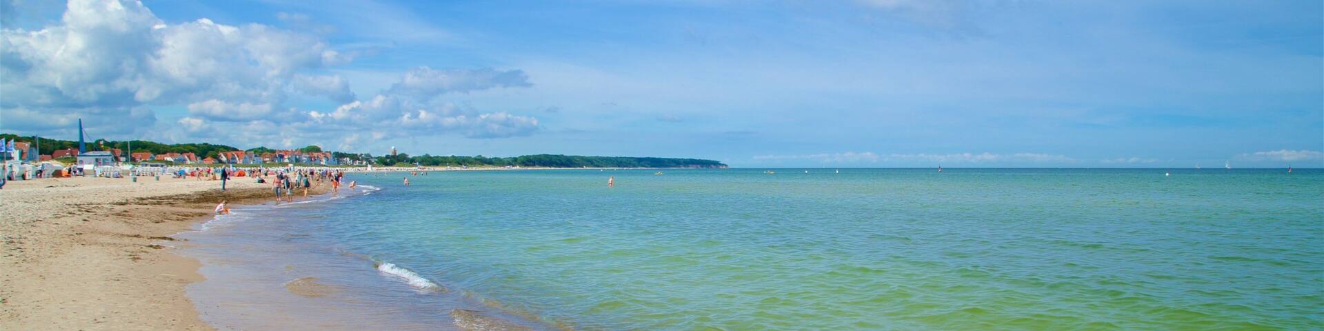 A beach with clear water, a sandy shore, and a distant shoreline with buildings.