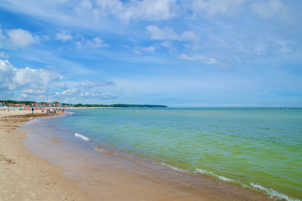 Uma praia com águas cristalinas, areia dourada e uma linha de costa distante com edifícios.