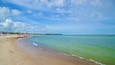 A beach with clear water, a sandy shore, and a distant shoreline with buildings.
