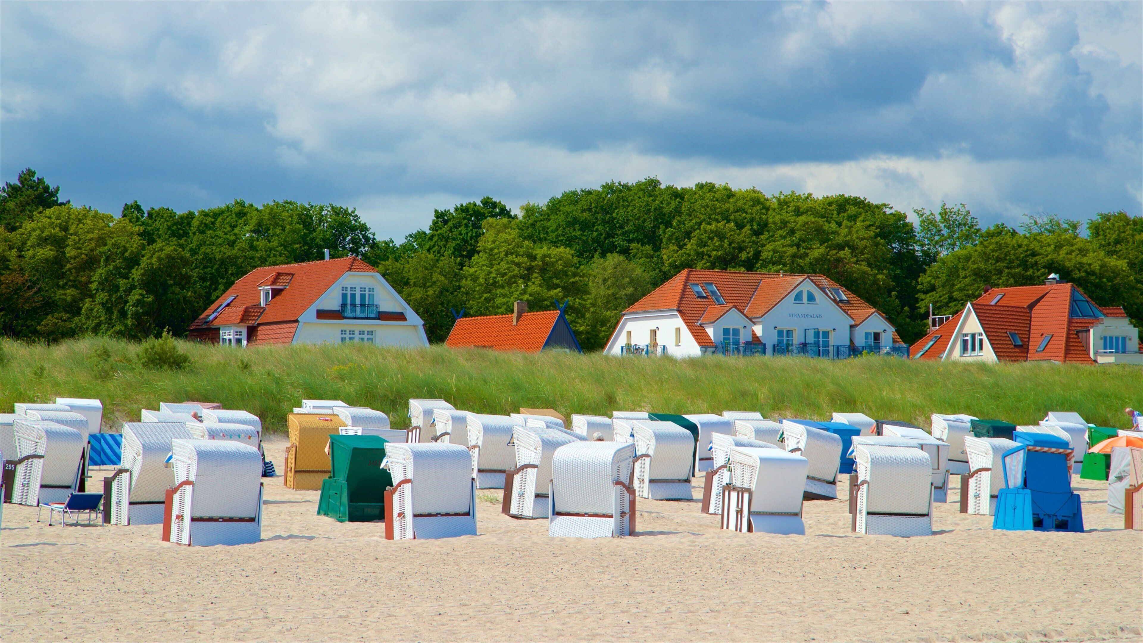 Beach chairs and houses on a sandy beach with a cloudy sky.
