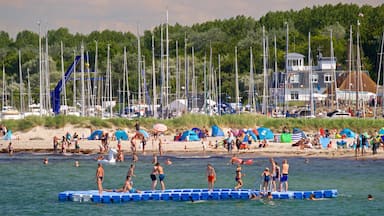 A beach with people swimming and standing on a floating platform. There are tents and a gazebo in the background.
