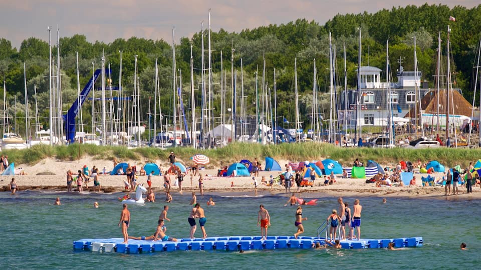 A beach with people swimming and standing on a floating platform. There are tents and a gazebo in the background.