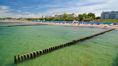 A beach with clear turquoise water, wooden groynes, and a row of blue beach umbrellas.