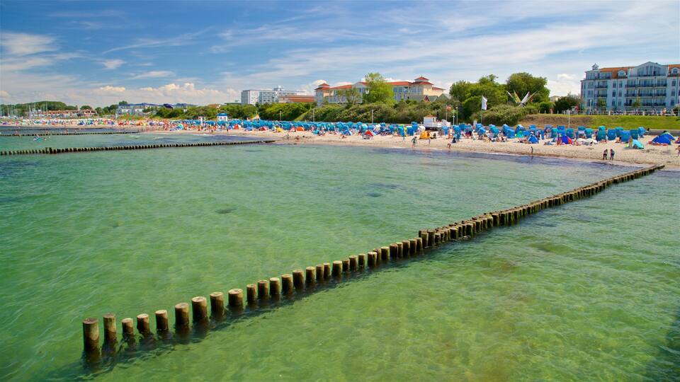 A beach with clear turquoise water, wooden groynes, and a row of blue beach umbrellas.