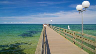 A wooden pier extending into a clear blue sea with people walking along it.