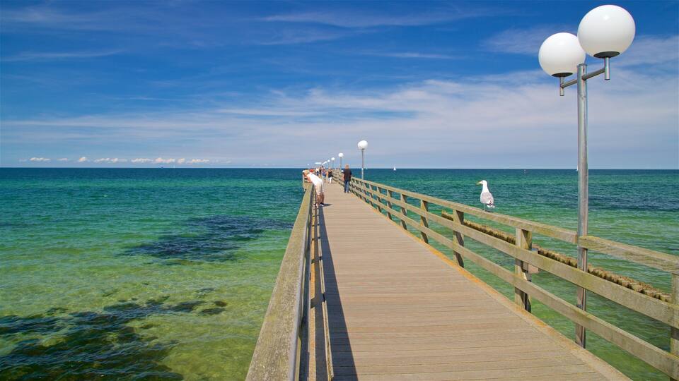 A wooden pier extending into a clear blue sea with people walking along it.