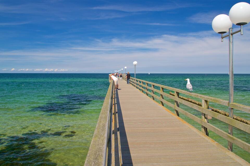 Eine Holzstele, die sich in ein klares, blaues Meer erstreckt, während Menschen darauf entlanggehen.