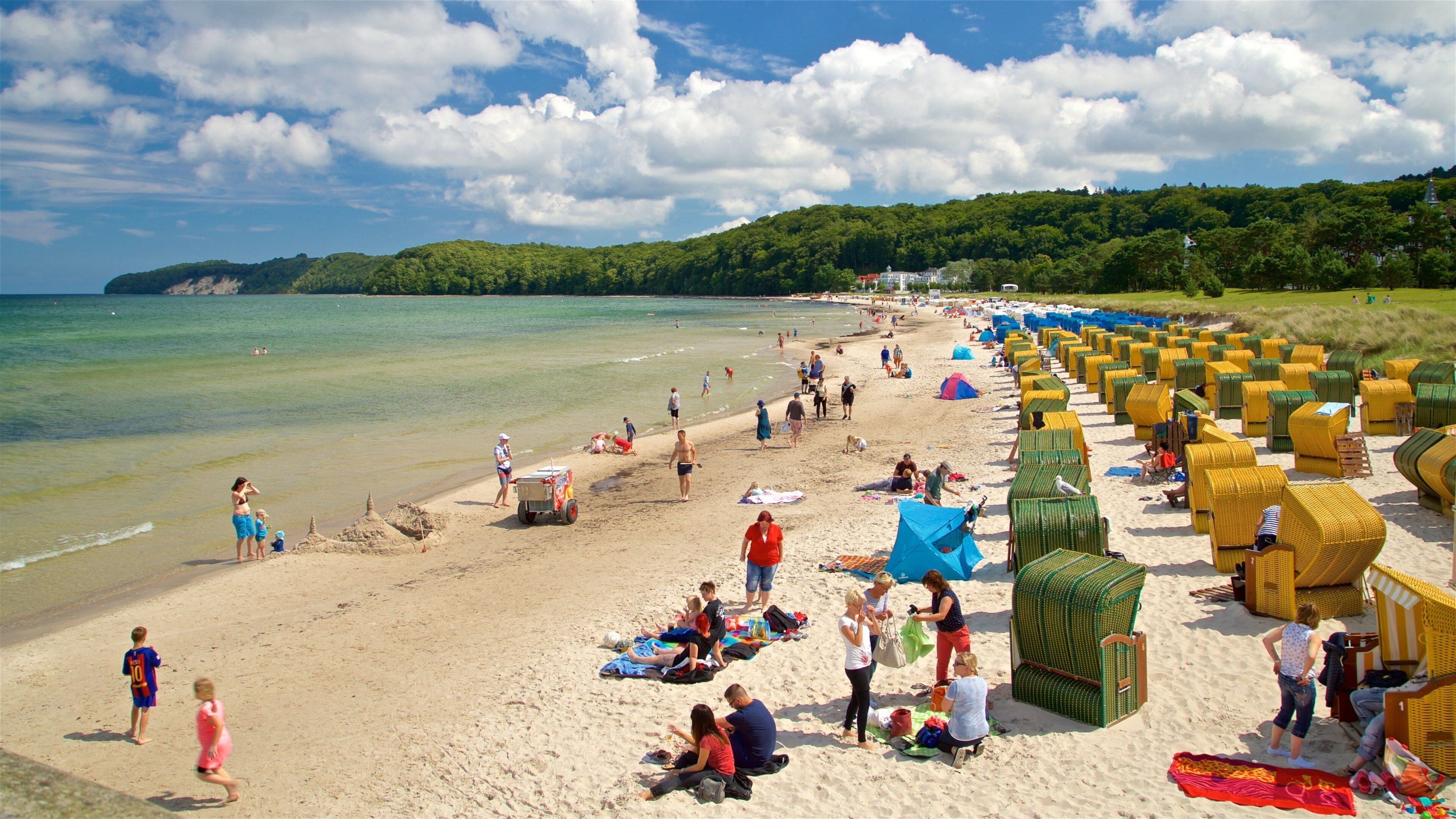 A beach with people, sand, water, and green hills in the background.