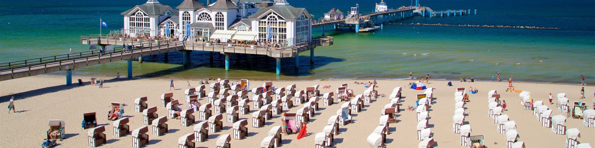A beach with rows of beach huts and a pier extending into the ocean.