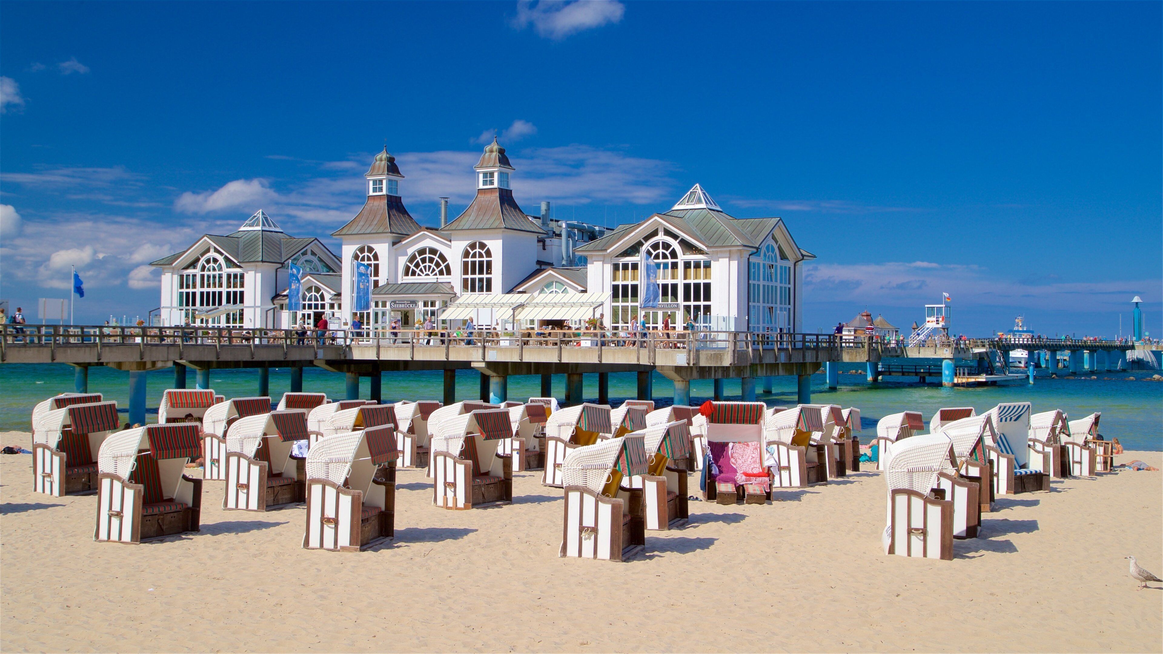 A pier with beach chairs and a white building with multiple windows and a flag.
