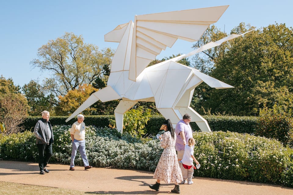 Un groupe de personnes se promène près d’une grande sculpture blanche dans un jardin planté d’arbres et d’arbustes.