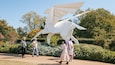 A group of people walking near a large white sculpture in a garden with trees and bushes.