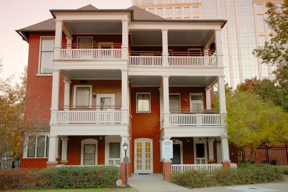 Un immeuble à plusieurs étages, doté d’une façade en briques rouges, de balcons blancs et d’une enseigne indiquant « Maison de Margaret Mitchell ».
