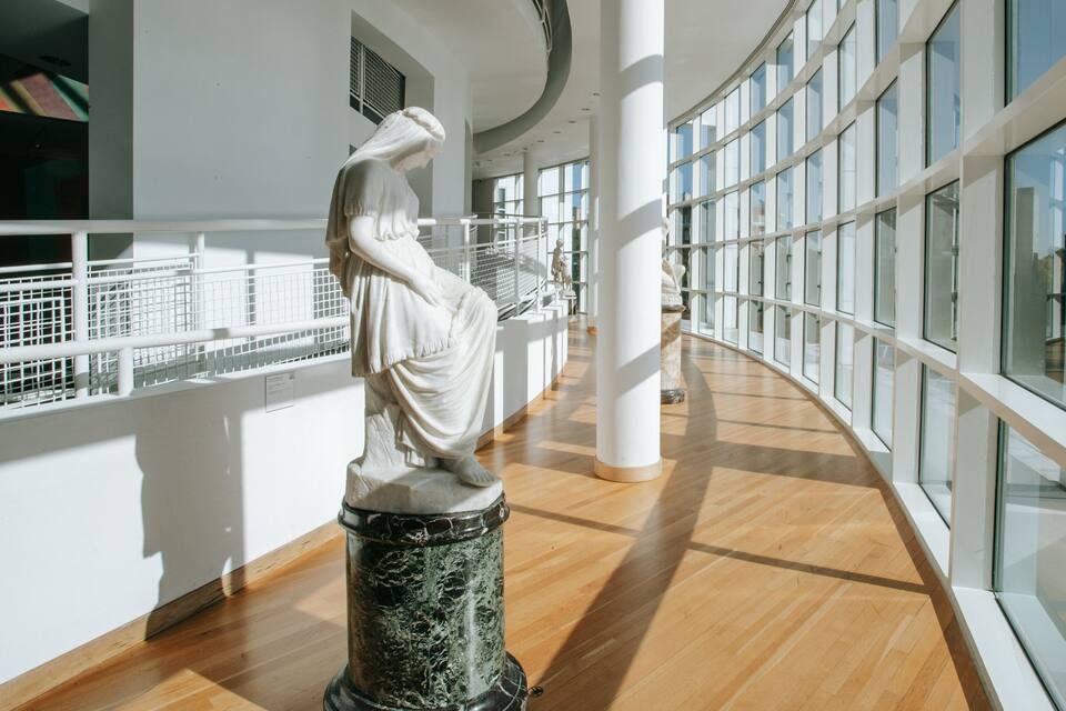 A marble statue in a modern building with large windows and wooden floors.