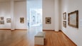 An art gallery with wooden floors, white walls, and several framed paintings.