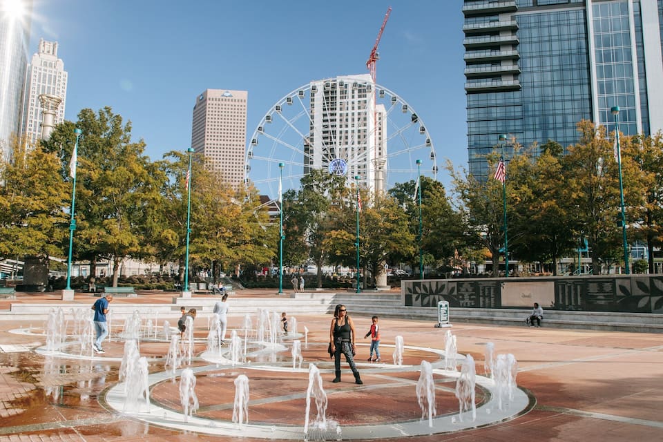 A city square with a water fountain, a Ferris wheel, and modern buildings.