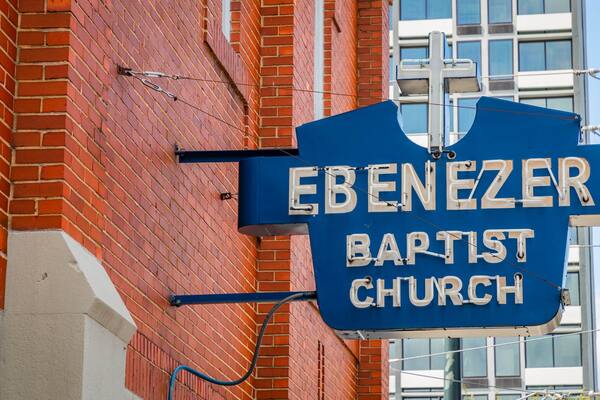 Ein blaues Schild mit weißer Beschriftung, auf dem 'EBENEZER BAPTIST CHURCH' steht, an einer Backsteinmauer befestigt.