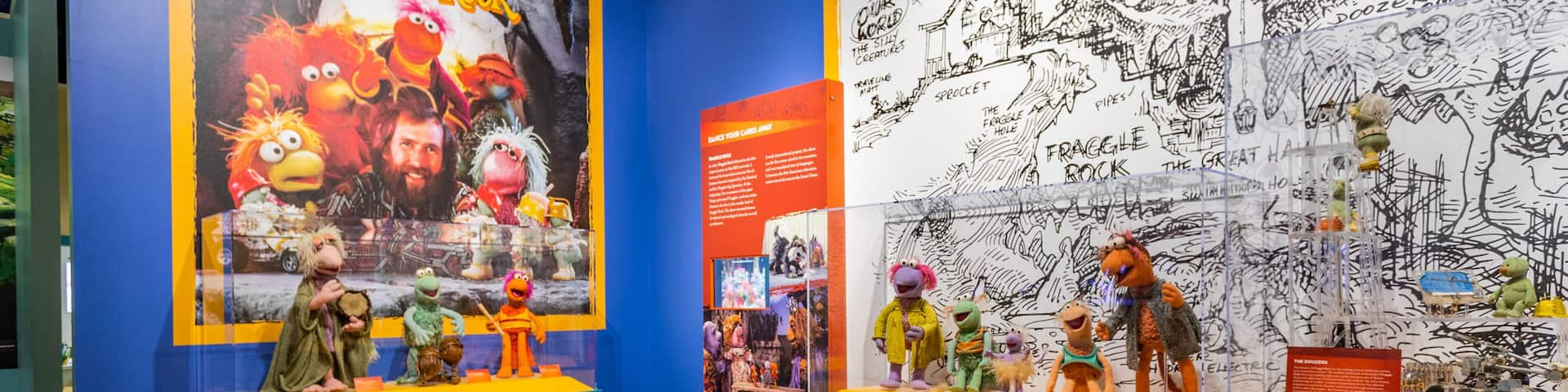 A museum exhibit with Muppet characters and a wall with hand-drawn sketches.