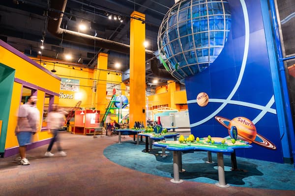 An indoor play area with colorful walls, a large globe, and tables with green and yellow objects.