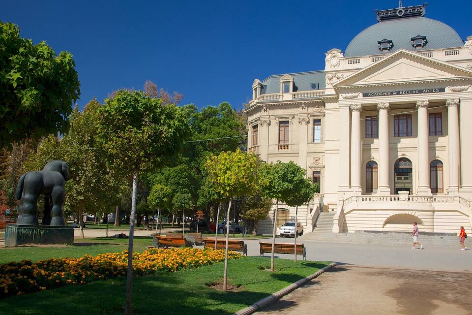 A large building with a dome and columns, surrounded by trees and a statue.