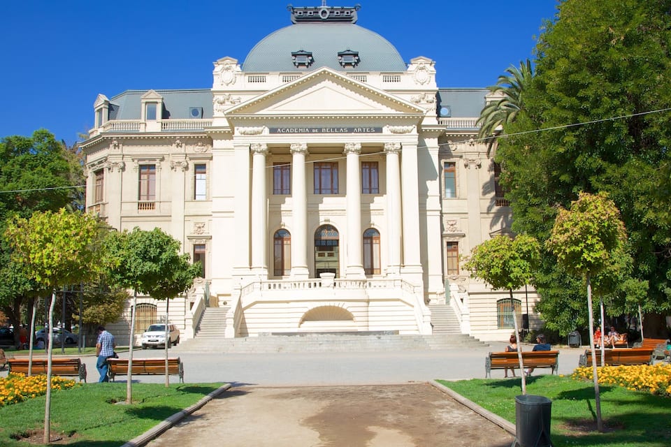 A grand building with a dome and columns, surrounded by trees and benches.