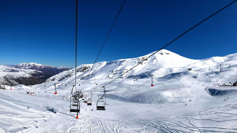 Panorama view of ski resort, slope, people on the ski lift, skiers on the piste among white snow in Valle Nevado near Santiago de Chile. Winter season extreme sports in South America.