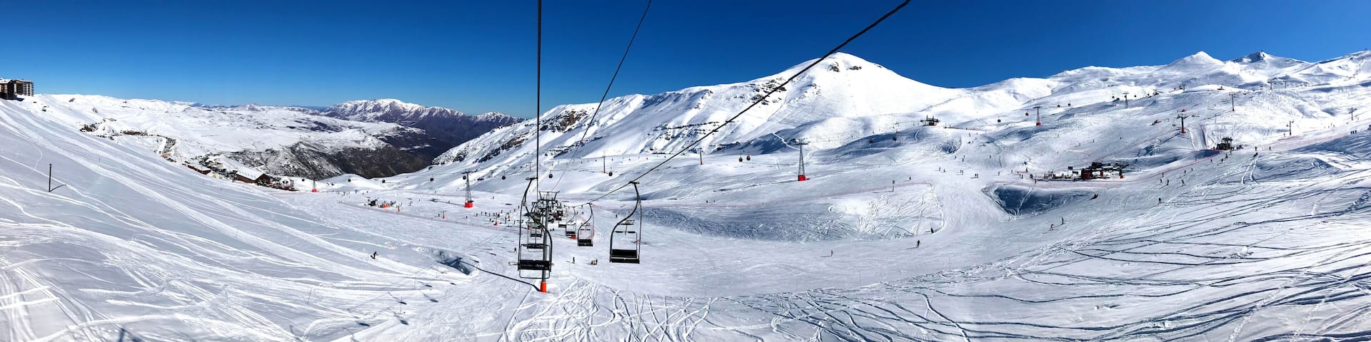Panorama view of ski resort, slope, people on the ski lift, skiers on the piste among white snow in Valle Nevado near Santiago de Chile. Winter season extreme sports in South America.