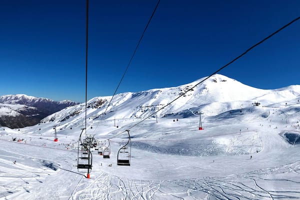 Panorama view of ski resort, slope, people on the ski lift, skiers on the piste among white snow in Valle Nevado near Santiago de Chile. Winter season extreme sports in South America.