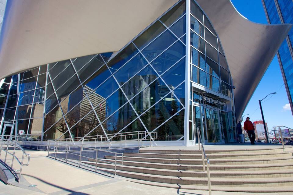 A modern glass building with a unique angular design, featuring a staircase leading to the entrance.